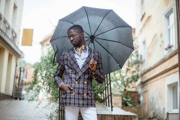 Confident young African man in a stylish suit with umbrella on city street - Фото, зображення