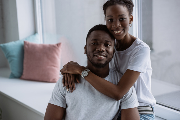 heureux jeune couple afro-américain en t-shirts blancs souriant à la caméra à la maison
  - Photo, image