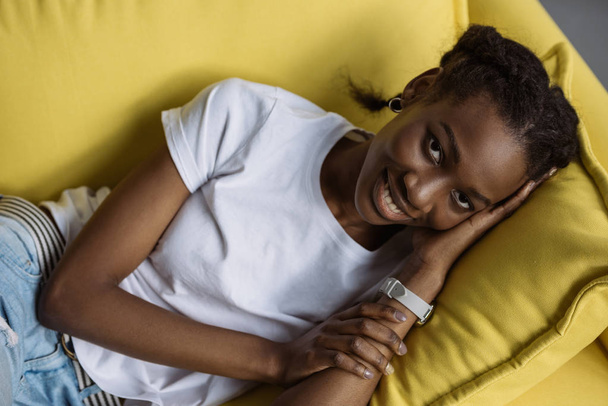 beautiful young african american woman lying on sofa and smiling at camera - Fotó, kép