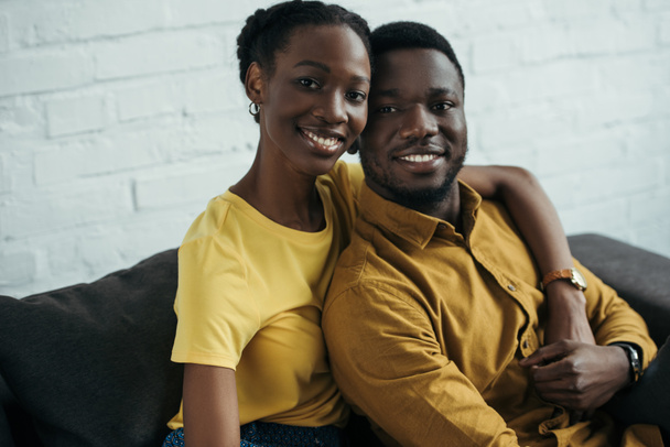 счастливая молодая африканская американская пара в желтых рубашках обнимающая и улыбающаяся в камеру
 - Фото, изображение