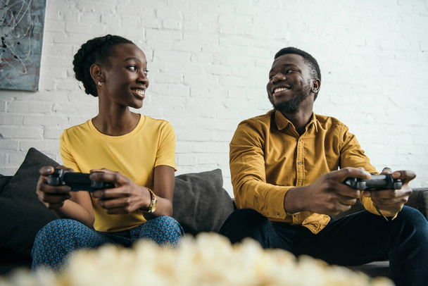 heureux jeune couple afro-américain jouer avec joysticks et regarder les uns les autres
 - Photo, image