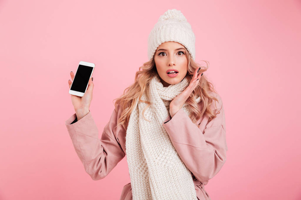 Shocked young woman wearing warm scarf showing phone - Foto, afbeelding