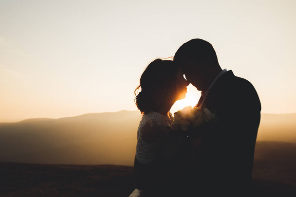 Ευτυχισμένο όμορφο γαμήλιο ζευγάρι νύφη και γαμπρός την ημέρα του γάμου σε εξωτερικούς χώρους στο βράχο βουνά. Ευτυχισμένο ζευγάρι γάμος σε εξωτερικούς χώρους για τη φύση, μαλακό ηλιόλουστα φώτα - Φωτογραφία, εικόνα