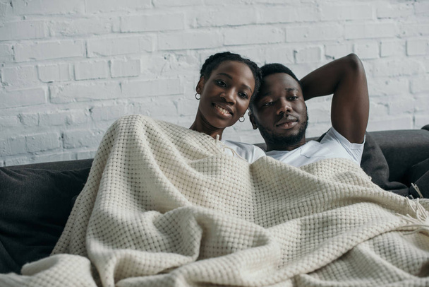 beautiful happy young african american couple lying together under blanket - Zdjęcie, obraz