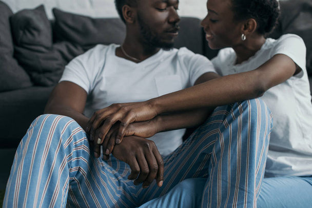 家庭でお互いに笑みを浮かべてのパジャマを着て美しい若いアフリカ系アメリカ人カップルのショットをトリミング   - 写真・画像