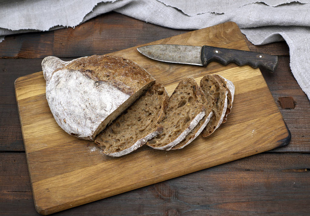 sliced bread with rye flour flour on a brown wooden board - Foto, Imagem