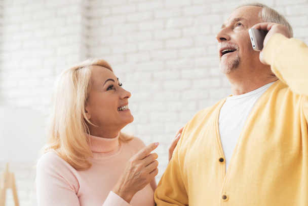 Ein Mann in einer gelben Strickjacke telefoniert. Neben ihr steht eine Frau im rosafarbenen Pullover und lächelt. Sie freut sich über gute Nachrichten. - Foto, Bild