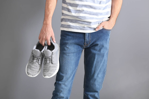 Hombre sosteniendo zapatos deportivos sobre fondo gris
 - Foto, Imagen