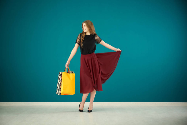 Beautiful young woman with shopping bags against color wall - Photo, image