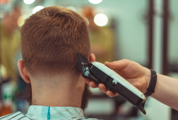 men's hairstyling and haircutting with hair clipper in a barber shop or hair salon. Soft focus. - Photo, image