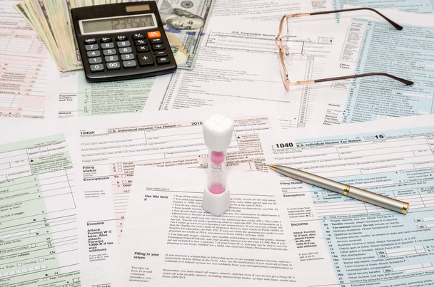 Ampulheta com formulário fiscal 1040, calculadora, caneta e notas de dólar
 - Foto, Imagem