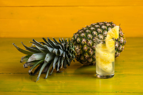 Kypsä ananas ja mehu lasissa keltaisella puisella backgrounilla
 - Valokuva, kuva