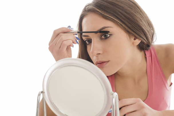 Nuori nainen laittaa ripsiväriä silmäripsiinsä. eristetty valkoisella pohjalla
 - Valokuva, kuva