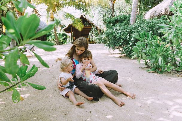 mladá matka s roztomilé malé dcery relaxační v tropické pláže - Fotografie, Obrázek