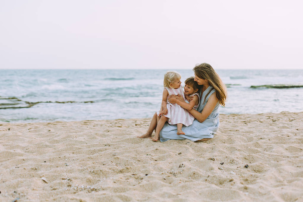 junge Mutter mit süßen kleinen Töchtern posiert am Sandstrand am Meer, Rückseite - Foto, Bild