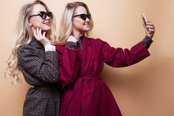  happy two smiling girls making selfie photo on smartphone on beige background - Zdjęcie, obraz