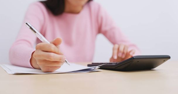 Mujer usando calculadora y escribiendo en papel
  - Foto, Imagen