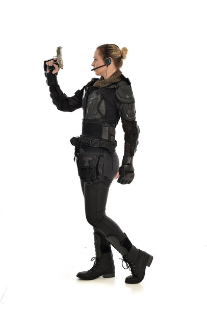 Tam boy siyah taktik zırh giyen, beyaz stüdyo arka plan üzerinde izole bir silah tutan kadın asker portresi. - Fotoğraf, Görsel