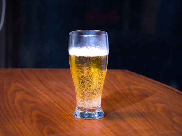 Fotografía de una pinta de cerveza light lager sobre un tablero de madera de nogal negro con fondo oscuro
. - Foto, imagen