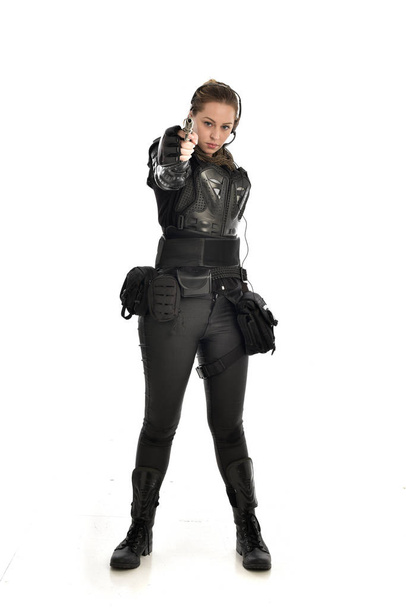 戦術的な黒の鎧を着て、白いスタジオ背景に分離された銃を保持している女性兵士の完全な長さの肖像画. - 写真・画像