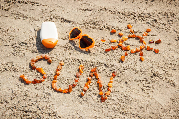 Word and shape of sun, sunglasses with sun lotion on sand at beach, summer time concept - 写真・画像