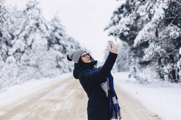 Ένα όμορφο κορίτσι κάνει μια selfie στη μέση ένα χιονισμένο δάσος roa - Φωτογραφία, εικόνα
