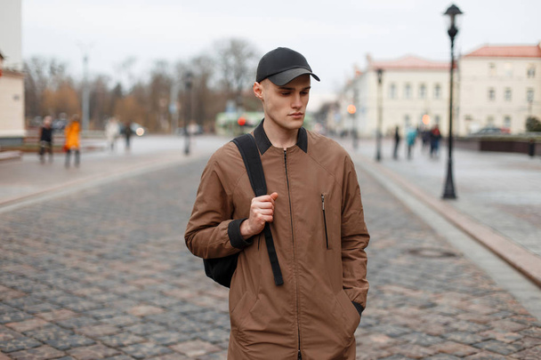 Young stylish man in a trendy fashion coat with a cap and a back - Fotoğraf, Görsel