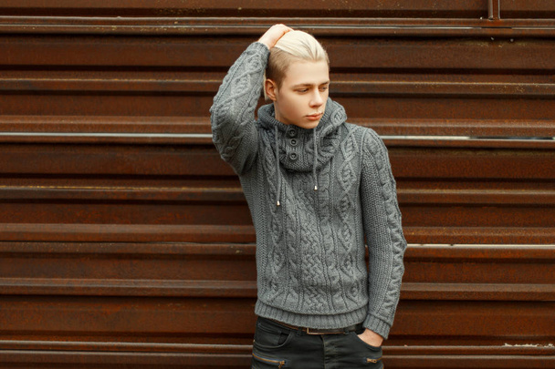 Красивий молодий чоловік у в'язаному светрі позує біля металевої стіни
 - Фото, зображення
