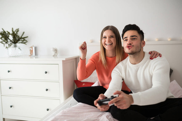 Happy couple sitting on bed playing video games - Valokuva, kuva