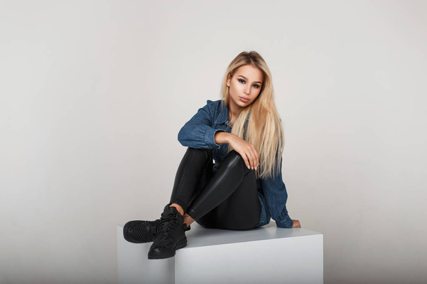 Young woman in fashion denim clothes with stylish shoes sits - Valokuva, kuva
