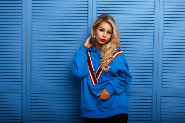 Sexy beautiful young woman with stylish make-up in a fashion blue sweatshirt near a wooden wall - Photo, Image