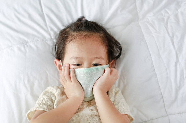 Little girl wearing a protective mask lying on the bed. - Foto, immagini