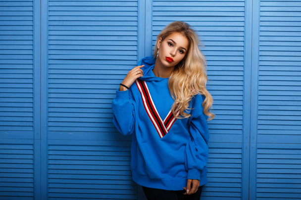 Beautiful young girl with red lips in fashionable blue clothes near a wooden wall - Photo, Image