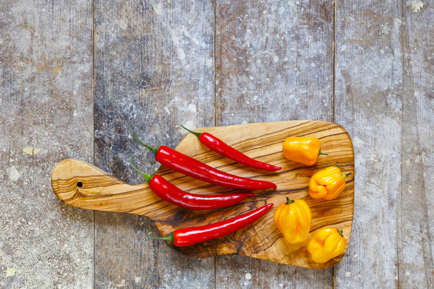 Red and yellow hot peppers on cutting board on old wooden table with copy space above - Foto, afbeelding