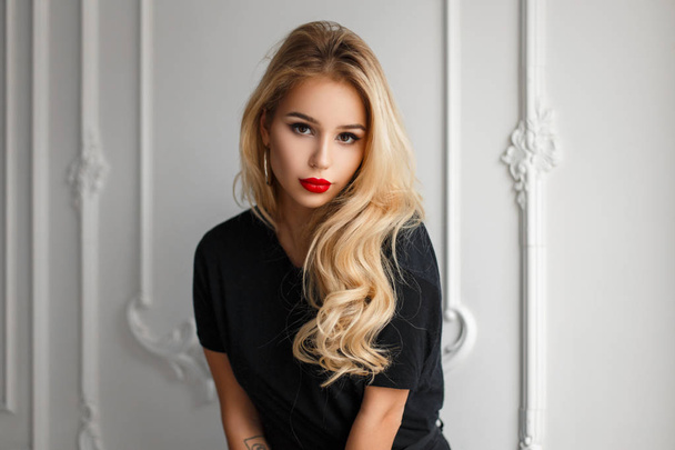 Sexy mujer joven de moda con rizos en una camiseta de moda negra cerca de una pared blanca
 - Foto, imagen