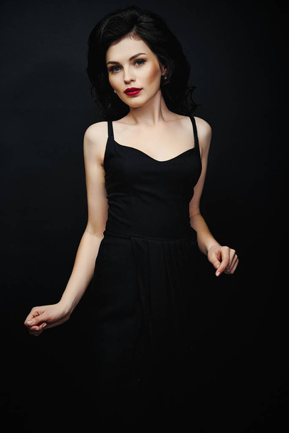 Gorgeous young brunette woman in elegant black dress posing against dark studio background  - Foto, Bild
