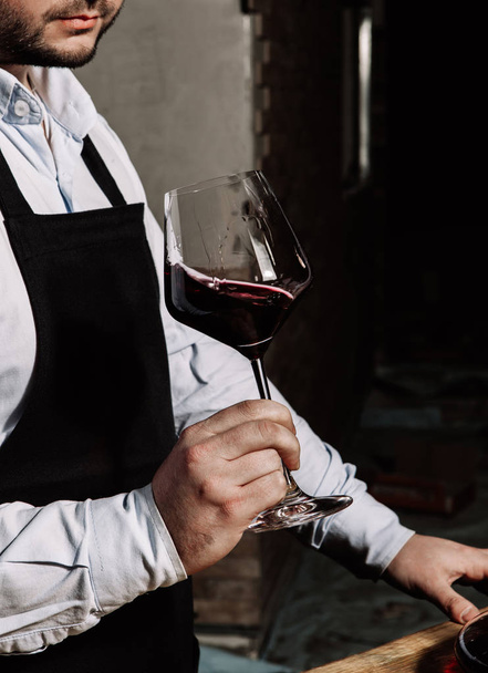 sommelier w czarny fartuszek i lekkich bluzek, trzymając kieliszek czerwonego wina - Zdjęcie, obraz