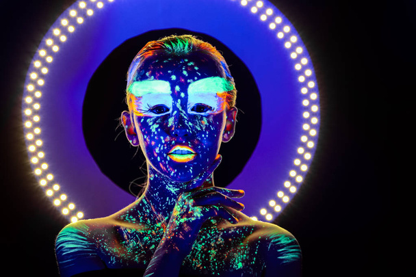 Portrait of beautiful girl with ultraviolet paint on her face. Girl with neon make-up in color light. - Zdjęcie, obraz