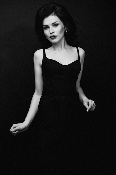 black and white photo of gorgeous young brunette woman in elegant black dress posing against  studio background  - Fotografie, Obrázek