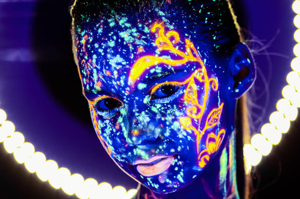 Portrait of beautiful girl with ultraviolet paint on her face. Girl with neon make-up in color light. - Fotografie, Obrázek