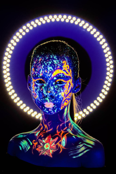 Portrait of beautiful girl with ultraviolet paint on her face. Girl with neon make-up in color light. - Fotó, kép