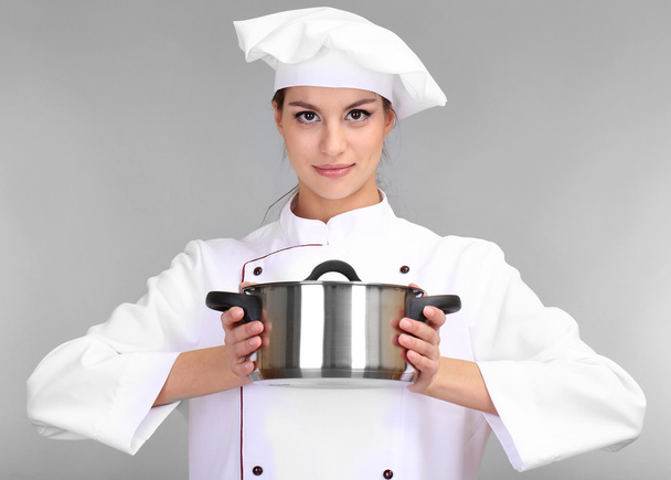 Portret van een jonge vrouw chef-kok met pan op grijze achtergrond - Foto, afbeelding