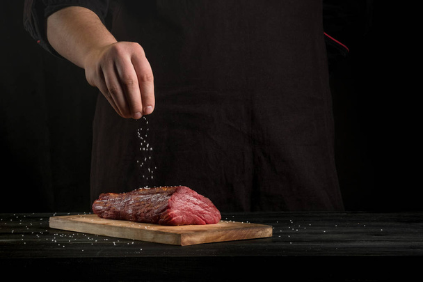 male hands prepare raw meat with spices on wooden board background    - Foto, afbeelding