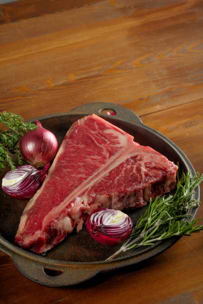 close-up de carne crua com cebola e alecrim em placa de metal na mesa de madeira
 - Foto, Imagem