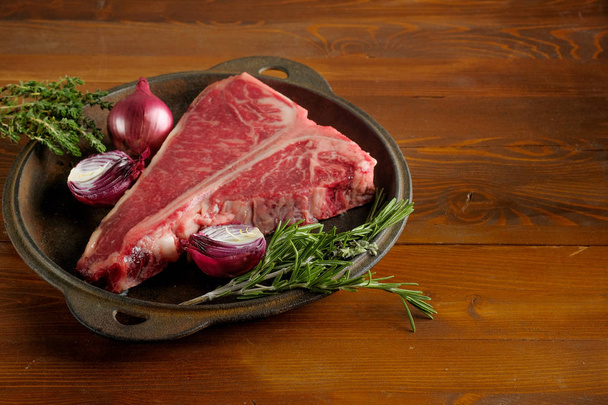 close-up de carne crua com cebola e alecrim em placa de metal na mesa de madeira
 - Foto, Imagem