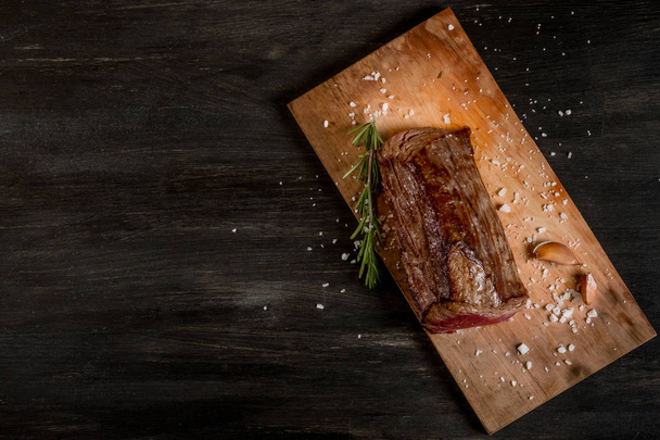 grilled meat with garlic and rosemary on wooden board on black table background    - Fotografie, Obrázek
