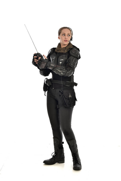 retrato de cuerpo entero de una soldado vestida con armadura táctica negra, sosteniendo un mando a distancia, aislada sobre fondo blanco del estudio
. - Foto, Imagen