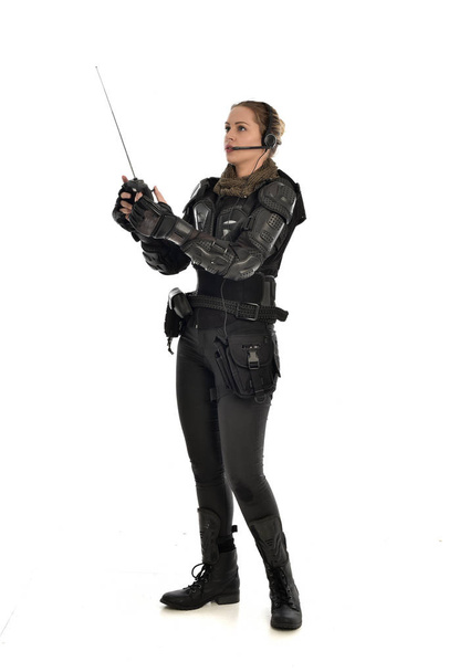 full length portrait of female  soldier wearing black  tactical armour, holding a remote control, isolated on white studio background. - Photo, Image