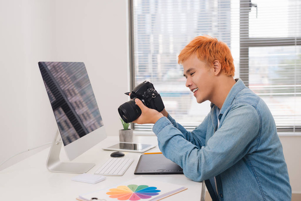 Αρσενικό φωτογράφος, κάθεται στο γραφείο του, ψάχνει για φωτογραφική μηχανή - Φωτογραφία, εικόνα