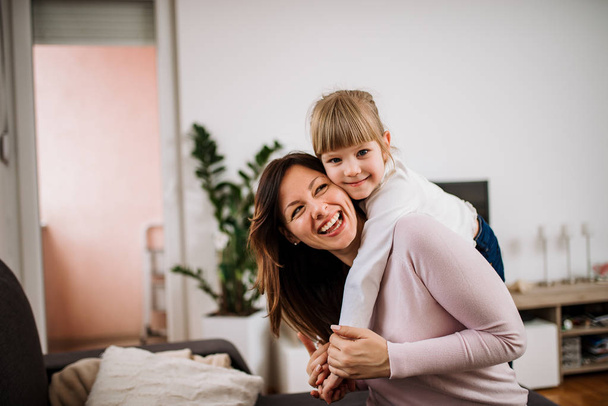 Portrait of happy mother piggybacking daughter at home - Фото, изображение